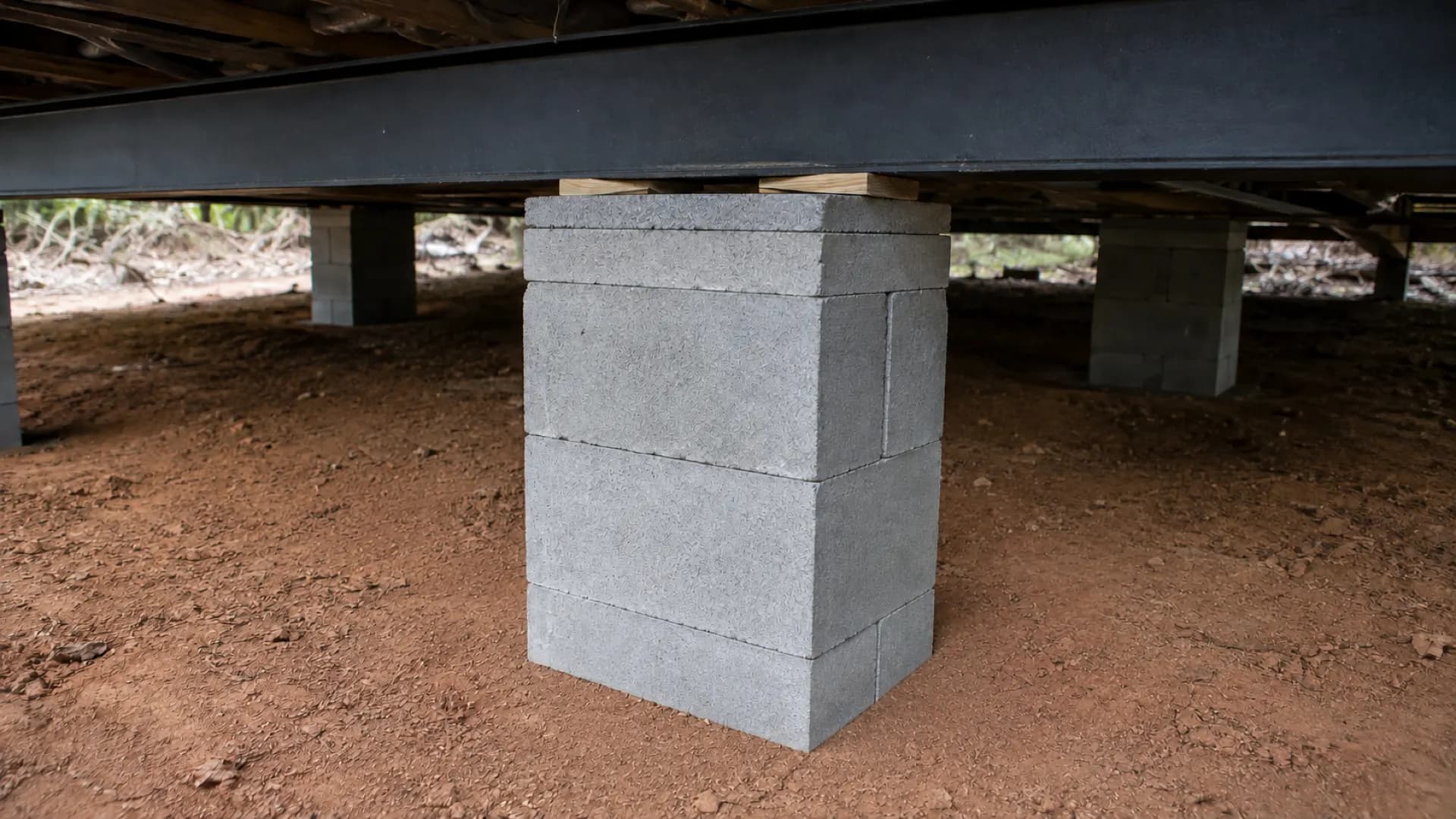 A block pier under a manufactured home frame: blocks stacked square with a cap block and wood wedges tight against the steel beam.