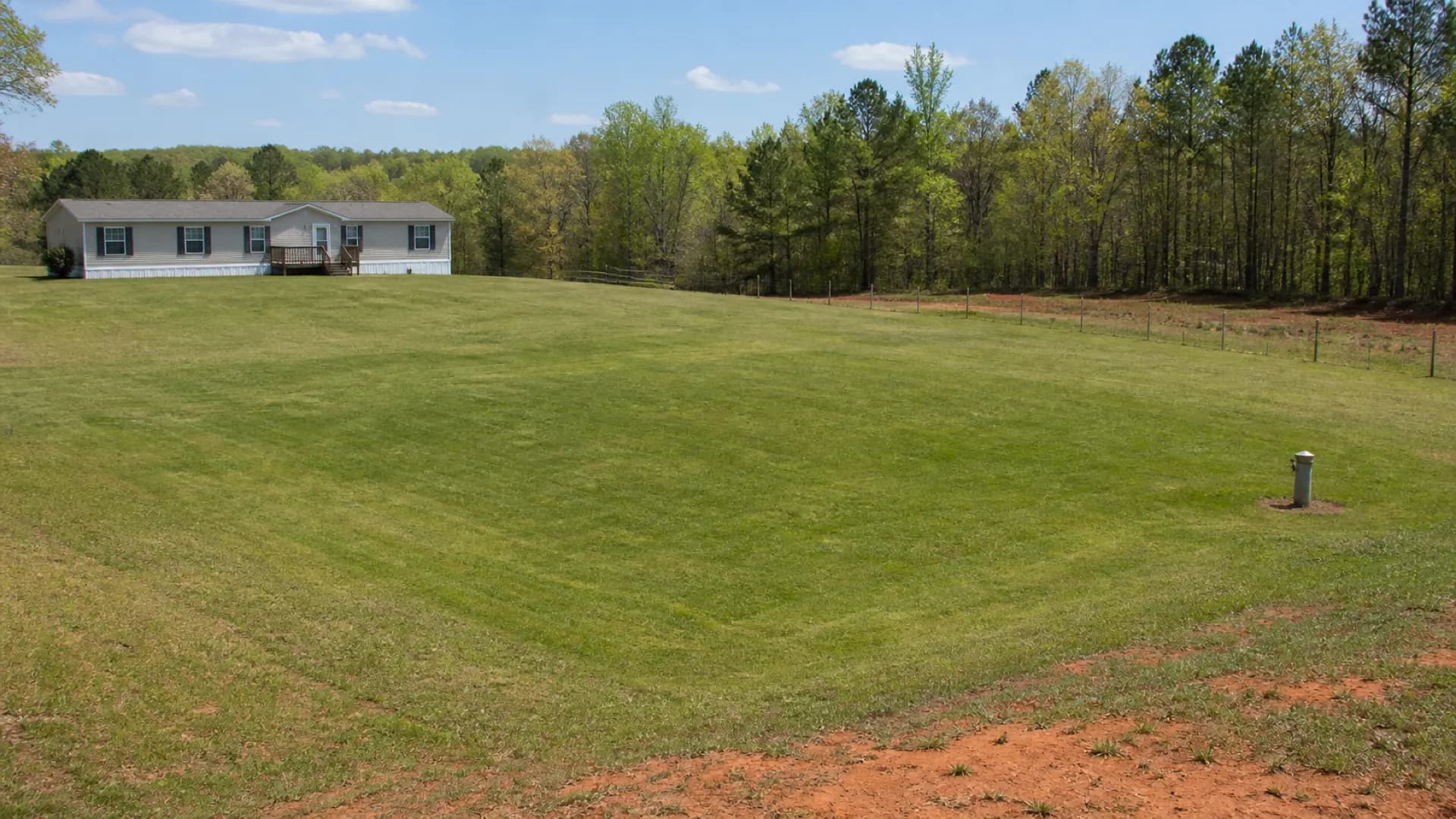 A level, mowed lawn over a septic drainfield beside a manufactured home, with only an inspection riser showing.