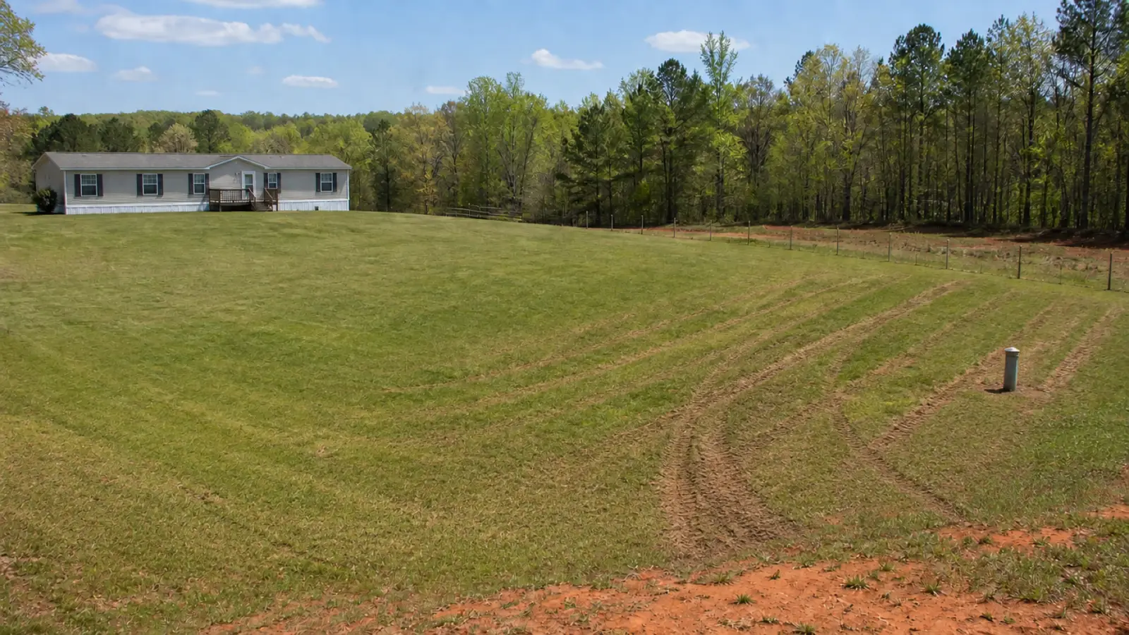 Tire ruts from a vehicle cut across the lawn over a septic drainfield beside a manufactured home.